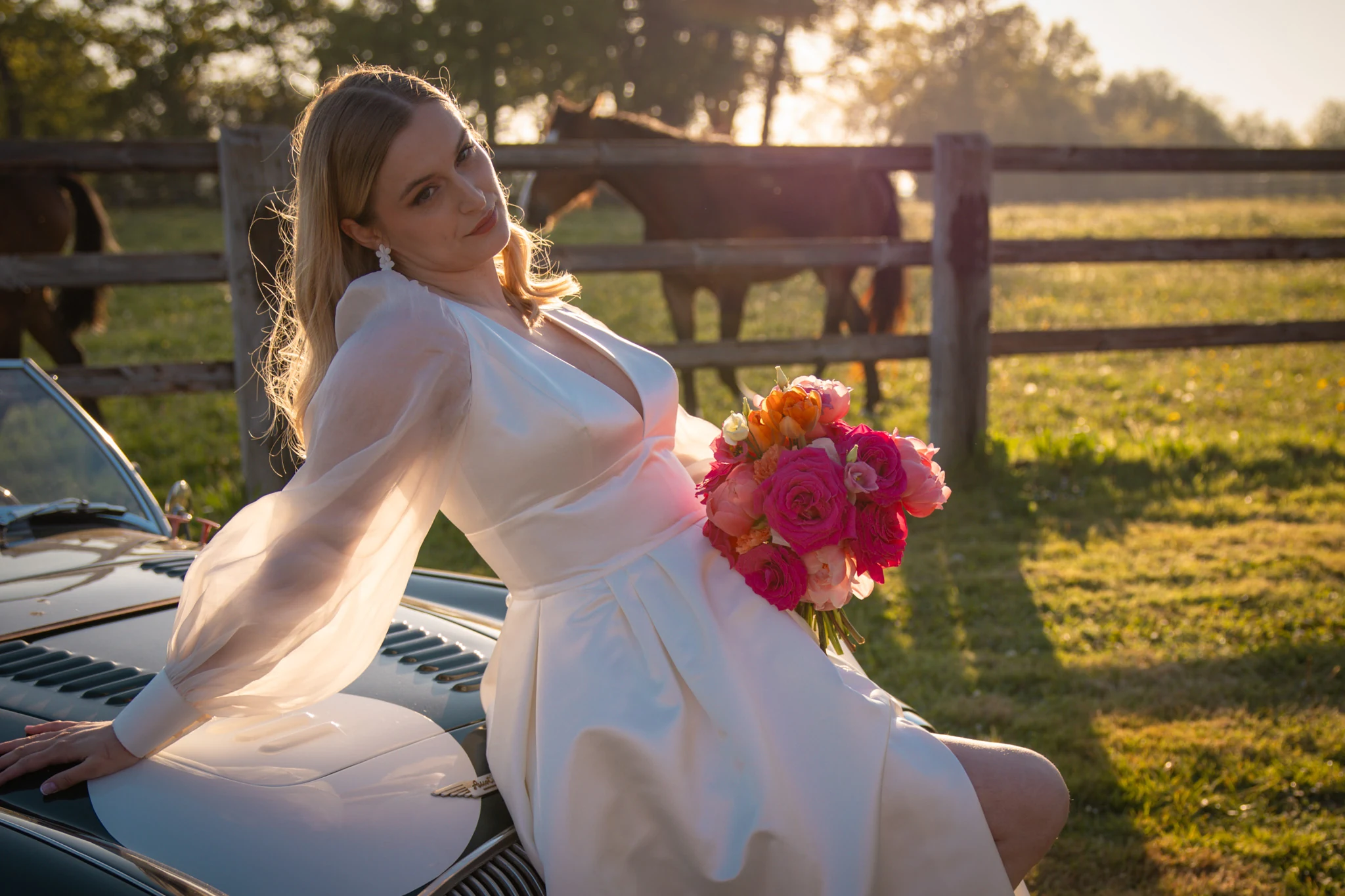 The bride sits by a car with her bouquet in hand