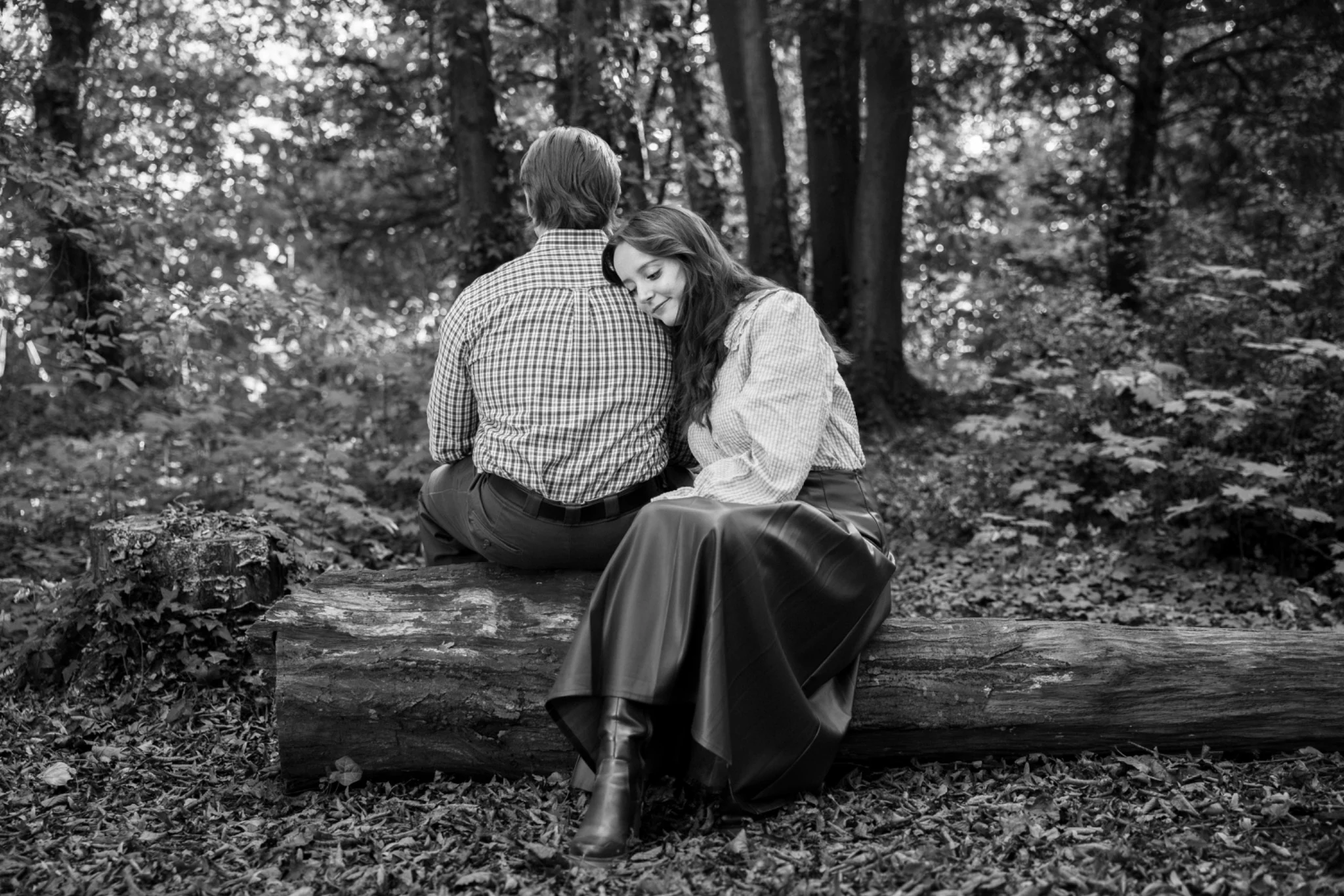 A couple shares a tender moment on a bench in the woods
